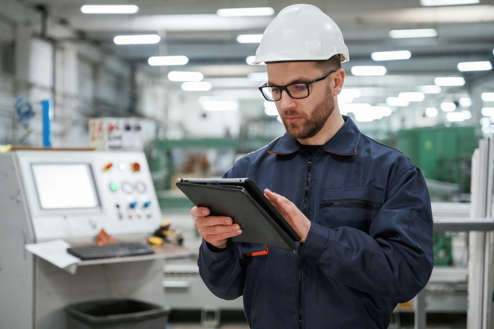 Holding,Tablet.,Factory,Worker,Is,Indoors,With,Hard,Hat.